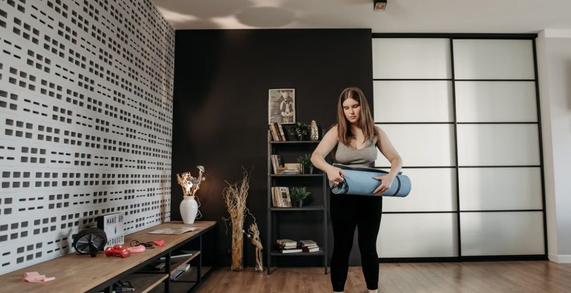 Plus size woman rolling a yoga mat in a stylish indoor setting with modern decor.