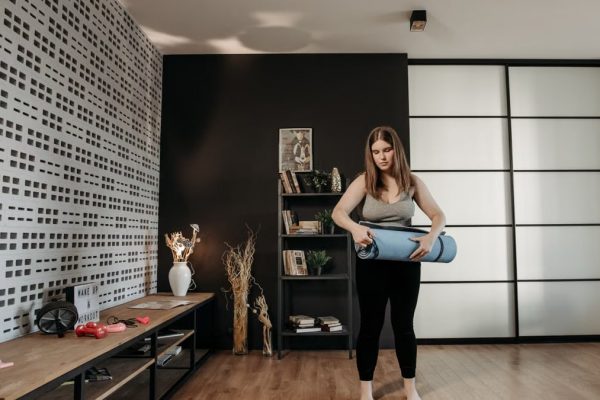 Plus size woman rolling a yoga mat in a stylish indoor setting with modern decor.